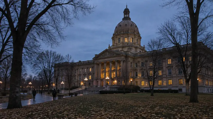 A domed legislature building at dusk in late autumn, fallen leaves on the lawn.